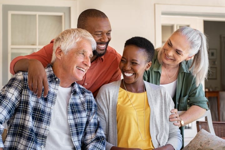 Cheerful friends sitting in courtyard enjoying the afternoon together. Group of four mature people sitting outside home and laughing. Happy senior man and old woman enjoying with mature african couple.